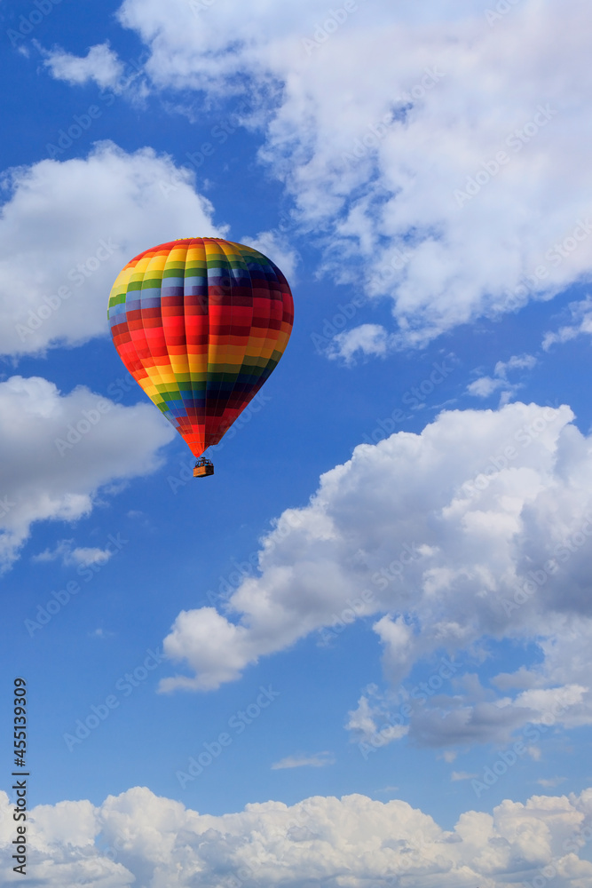A multicolored hot air balloon raises a basket with tourists in the blue sky. Vertical image. A multicolored hot air balloon raises a basket with tourists in the blue sky. Vertical image.