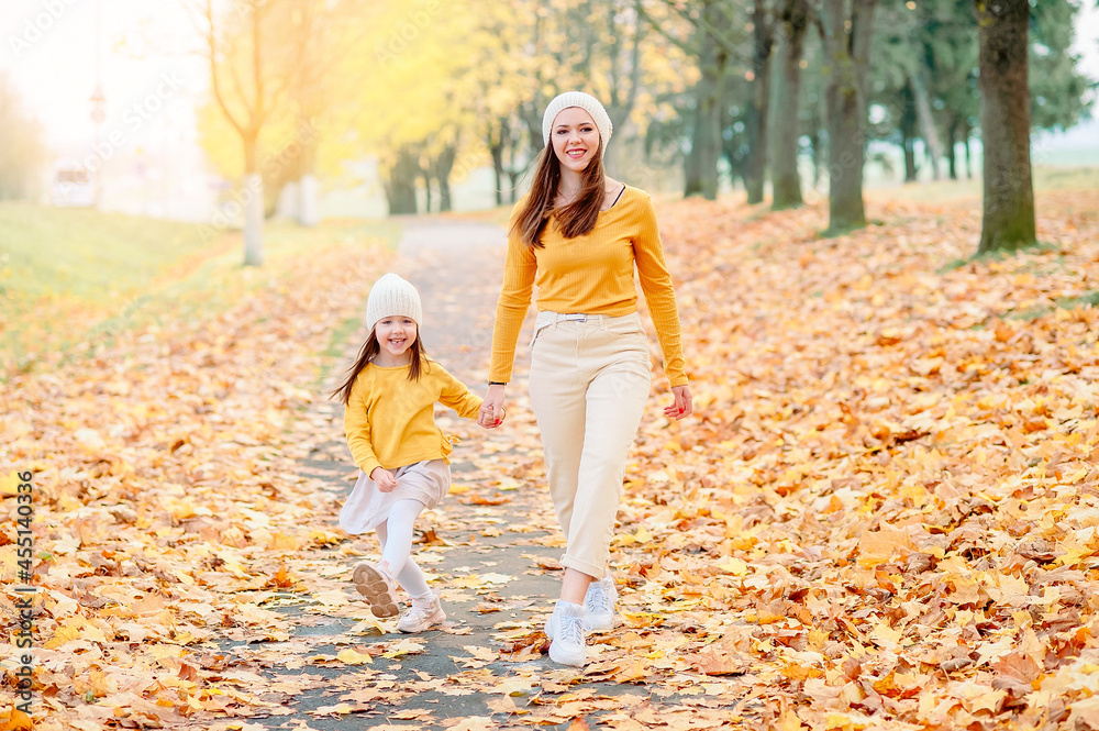 Fototapeta premium mom in a knitted hat with her daughter walking looking into the lens in the autumn park with a wide smile