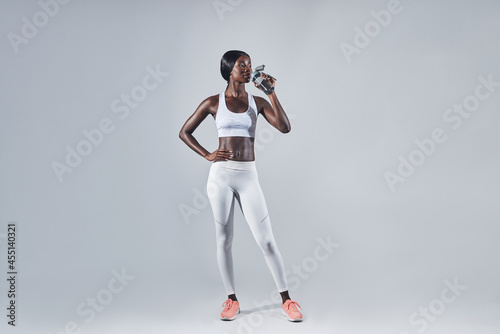 Full length of beautiful young African woman in sports clothing drinking water