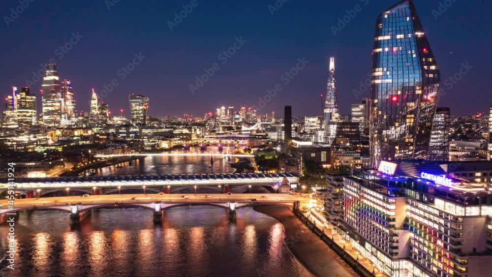 Aerial night hyperlapse footage of city. Forwards fly above Thames river at Blackfriars Bridge. Scene illuminated by city lights. London, UK