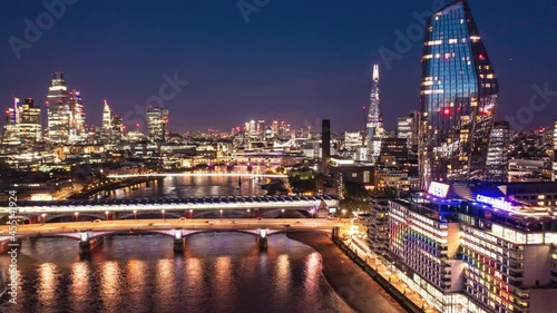 Aerial night hyperlapse footage of city. Forwards fly above Thames river at Blackfriars Bridge. Scene illuminated by city lights. London, UK photo