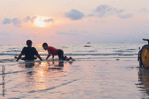Happy disabled teenage boy and wheelchair playing and relaxing with parent  Activity outdoors with father on the beach background  People having fun and diverse family concept.