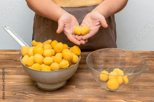 Caucasian woman chef peeling apricots fruits in bowl, preparing for making jam at home kitchen at summer autumn, online cooking, recipe instruction