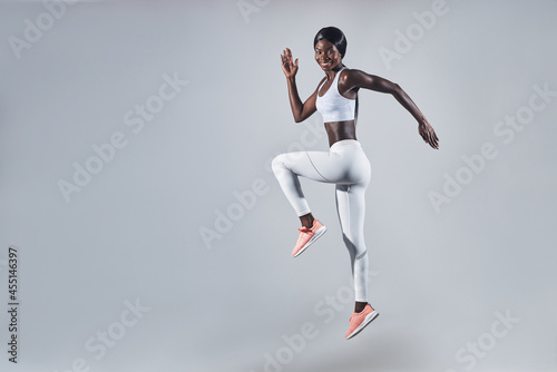 Full length of confident young African woman in sports clothing jumping against gray background
