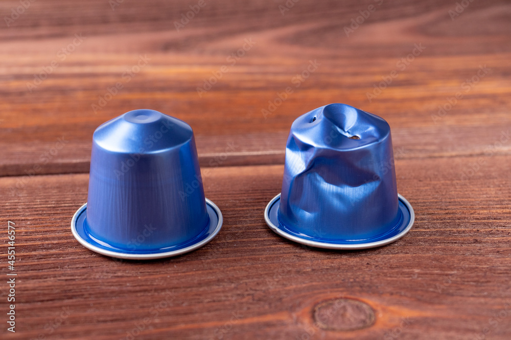 two blue aluminum capsules with ground coffee on a wooden background. One of them is already in use. Storage and processing of materials. Eco-friendly products two blue aluminum capsules with ground coffee on a wooden background. One of them is already in use. Storage and processing of materials. Eco-friendly products