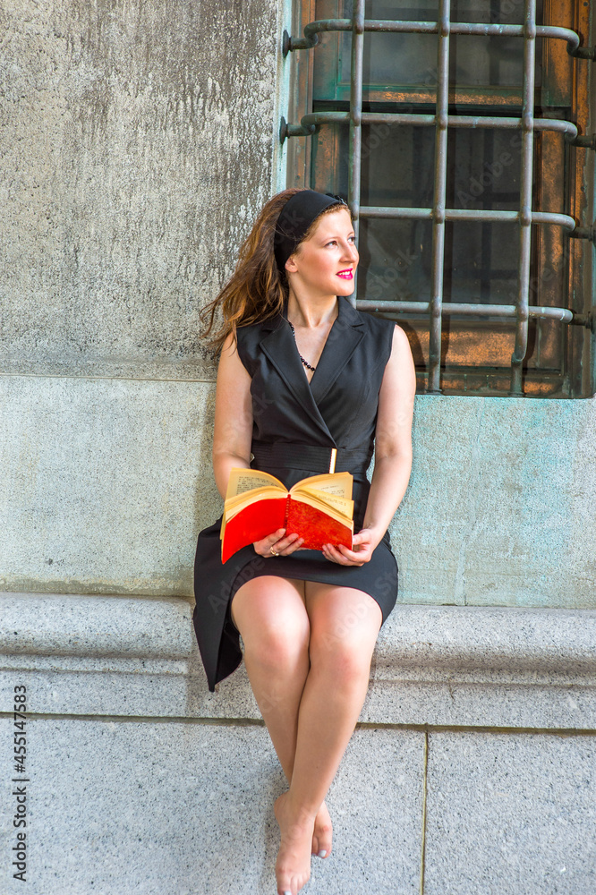 Sexy Woman Reading Outside. Wearing a black sleeveless trench coat dress, a  hair band, a young beautiful woman, barefoot, is sitting by a window,  smiling, looking up, reading a red book. Photos