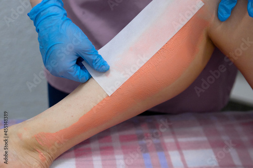 Epilation on the legs.Removal of unwanted hair on the legs.The master removes the wax with the help of special bandage strips for depilation.A girl in disposable gloves pasted a strip for depilation