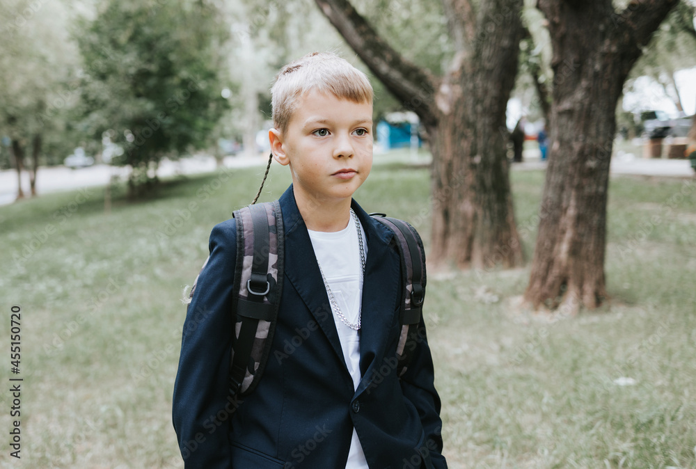 cute blond boy in a school uniform and with backpack on his shoulders goes to school at the beginning of the new school year, back to school concept and no desire to study cute blond boy in a school uniform and with backpack on his shoulders goes to school at the beginning of the new school year, back to school concept and no desire to study