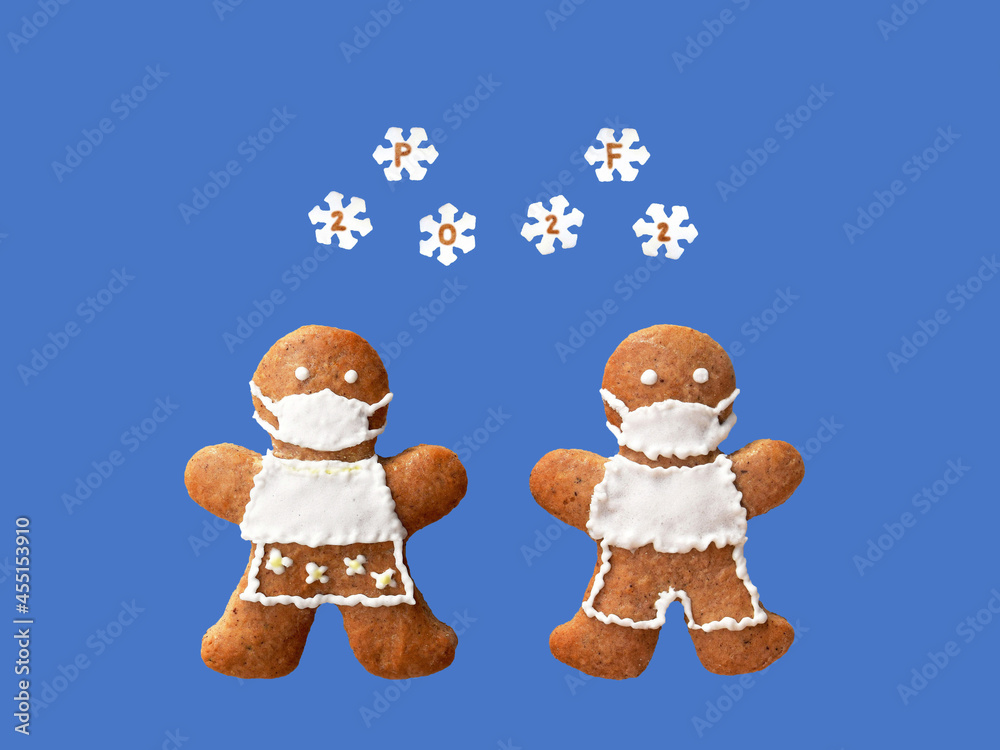 PF 2022 inscribed in snowflakes falling on gingerbread couple with protective face masks. Original New Year greeting card in coronavirus (COVID-19) time, isolated on blue background