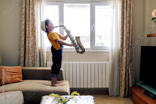 Girl playing saxophone on sofa in house room photo