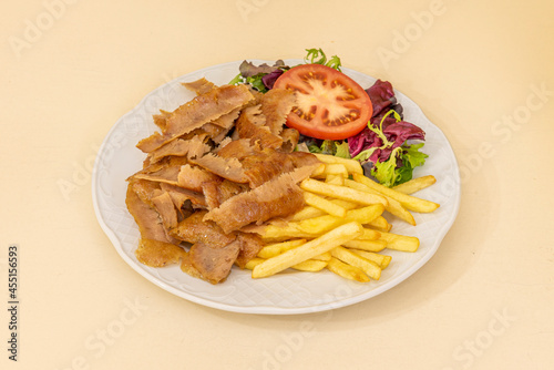 Kebab plate with spiced roast lamb slices, fried potatoes and oak salad and tomato slices in a restaurant doner kebab on white plate
