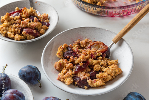 Foto Plum crumble dessert in plates with spoons on white background for tasty breakfa