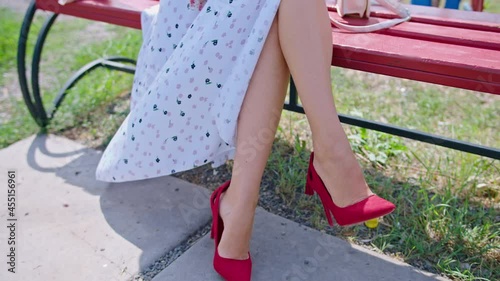 happy young woman sits on a bench in the park against the background of a red telephone booth, straightens her glasses. looking around. pinup.