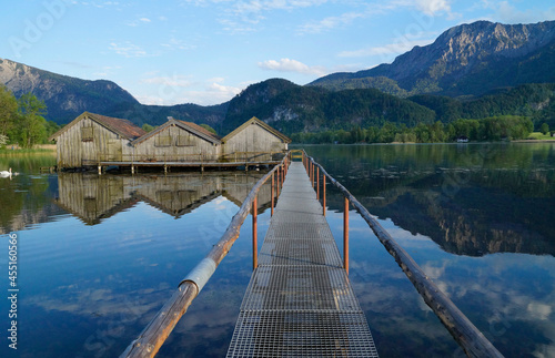 a pier leading to the wooden boat houses on serene lake Kochel  Kochelsee  with the scenic Bavarian Alps in the background reflected in the water  Bavaria  Germany 