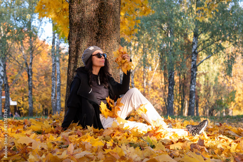 A girl sits in an autumn park and holds yellow maple leaves in her hand. Autumn mood. photo