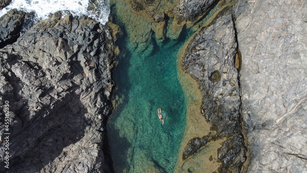 Persona nadando en una cala de mar con agua azul rodeado de rocas