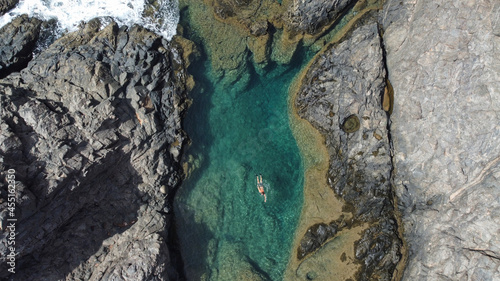 Obraz na płótnie Persona nadando en una cala de mar con agua azul rodeado de rocas w salonie