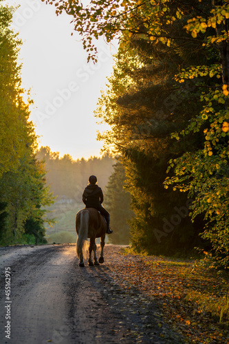 Woman horseback riding on the road at sunset