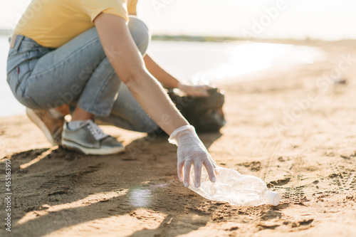 Close up Young female volunteer hand picking up trash, a plastic bottles and coffee cups, clean up beach with a sea. Woman collecting garbage. Environmental ecology pollution concept. Earth Day.