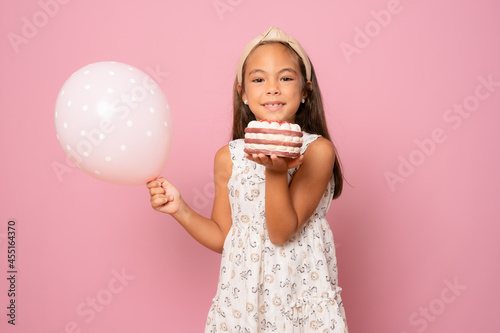adorable happy smiling little child girl with balloon celebrating with cake on pink background. birthday party.