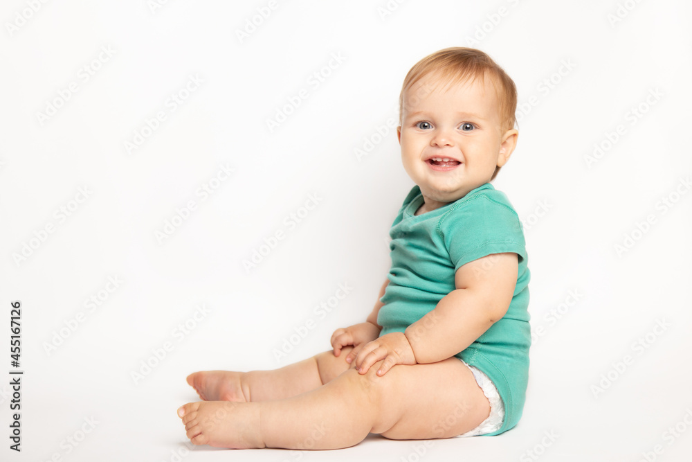Infant child baby boy wearing green t-shirt laughs happy looking at the camera isolated sitting on a white background. Childcare and upbringing concept. Infant child baby boy wearing green t-shirt laughs happy looking at the camera isolated sitting on a white background. Childcare and upbringing concept.