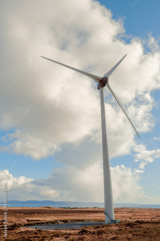 Wind farm tower with hub and rotor against blue cloudy sky. Warm sunny day. Green energy production.