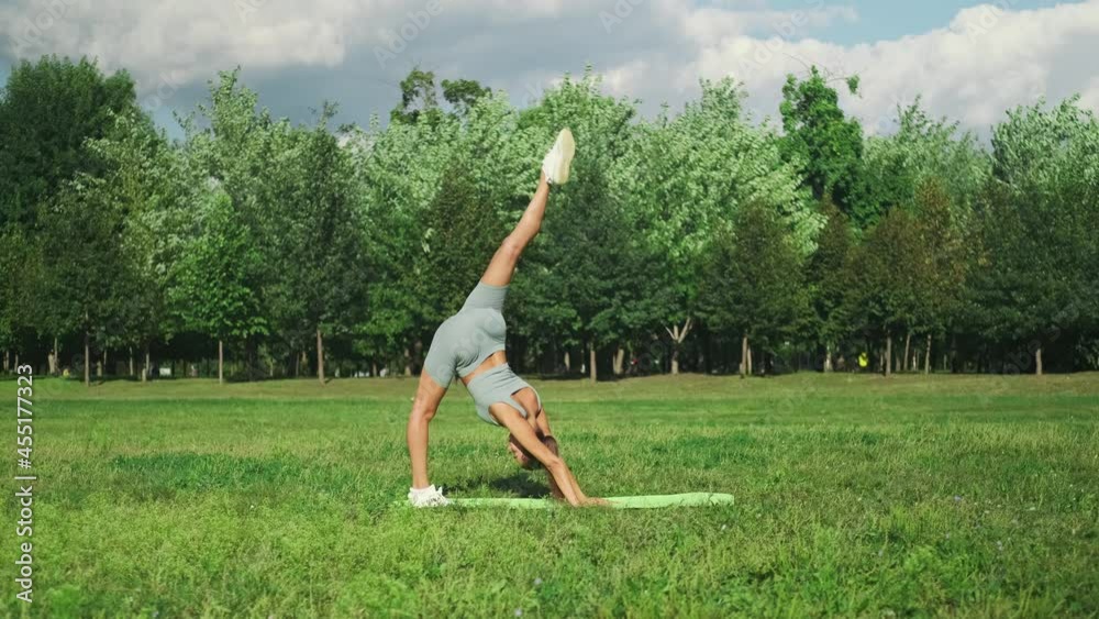A beautiful sportive girl is engaged in yoga on green grass in a city park. An outdoor gymnast is doing a series of exercises. Slow motion. 4k footage. A beautiful sportive girl is engaged in yoga on green grass in a city park. An outdoor gymnast is doing a series of exercises. Slow motion. 4k footage.