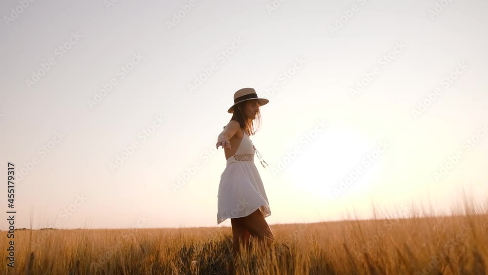 Happy free young woman dancing and spinning around in slow motion across field, touching ears of wheat with her hand. Wheat field on sunset background Happy free young woman dancing and spinning around in slow motion across field, touching ears of wheat with her hand. Wheat field on sunset background