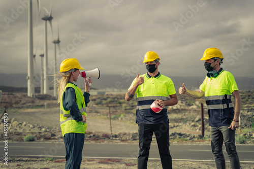 Engineer woman shouts over a megaphone. Skilled workers with protective mask, doing ok sign, thumb up with fingers. Electric central.