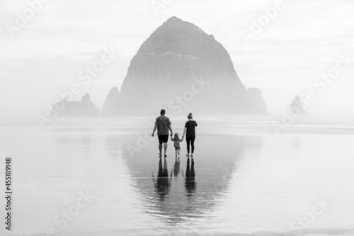 A family walking on the beach in the fog towards Haystack rock with a reflection