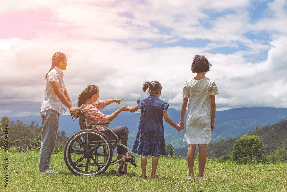 Group of female family with disabled woman in wheelchair and children standing on mountain park.Rear view Group of female family with disabled woman in wheelchair and children standing on mountain park.Rear view