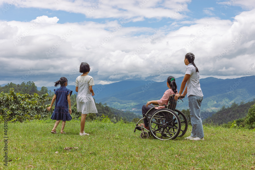 Group of female family with disabled woman in wheelchair and children standing on mountain park.Rear view Group of female family with disabled woman in wheelchair and children standing on mountain park.Rear view