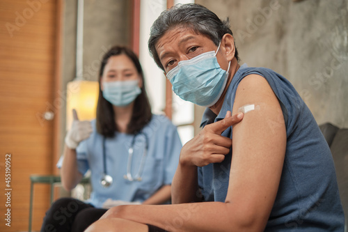 Elderly Asian male patient points a finger at a plaster-covered on his arm after vaccinating against COVID-19. This is a medical service from a specialist doctor at a retirement home.