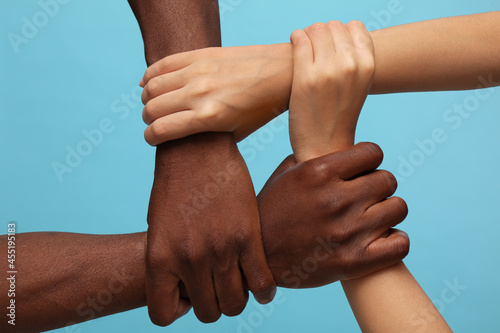 Woman and African American man joining hands together on light blue background, closeup photo