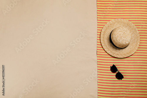 Striped beach towel, hat and sunglasses on sand, top view. Space for text