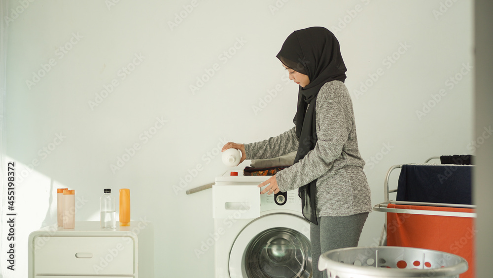 beautiful woman in hijab pours detergent for her laundry at home