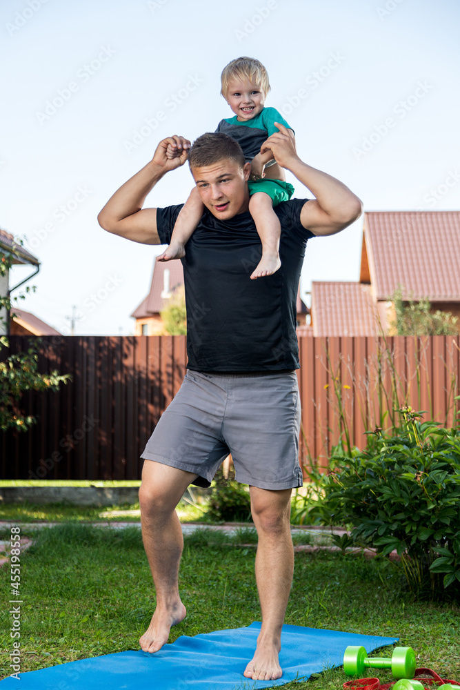 Obraz premium Happy young daddy is playing with her baby on a green lawn.Concept of a happy family. Fathers Day. Dad and son have activities together on holidays in backyard