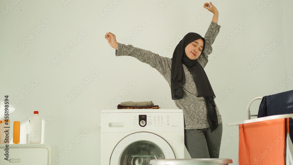 Asian woman in hijab unwinds after washing clothes at home