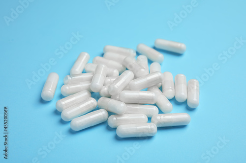 Pile of amino acid pills on light blue background, closeup