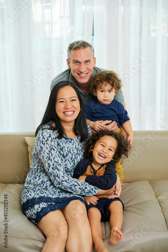 Obraz na plátne Happy joyful multi-ethnic family of four sitting on sofa at home and looking at