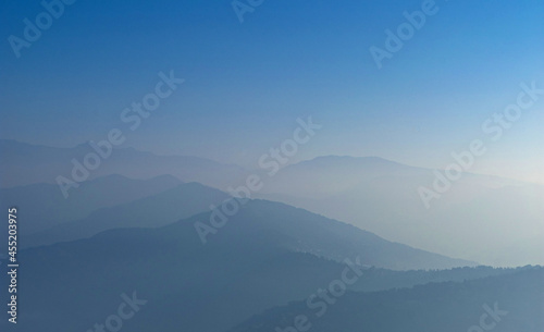 View of Himalayas mountain range with visible silhouettes through the colorful fog from Khalia top trek trail. Peaks of Himalayan mountains on the horizon.