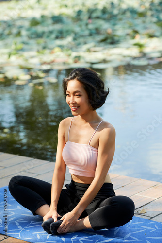 Happy slim fit young woman sitting on yoga mat in lotus position on wooden pier © DragonImages