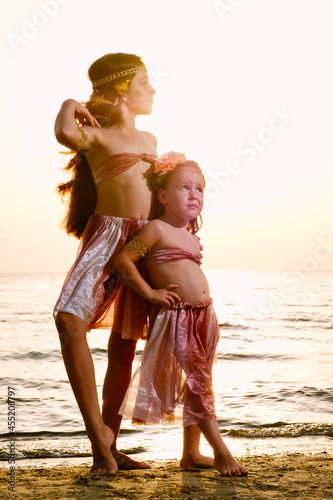 Two girls in the image of Moana at the sea in the rays of the sunset. photo