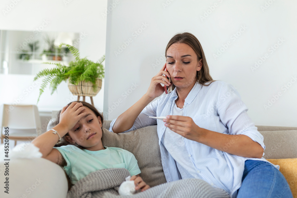 Mother measuring temperature of her ill kid. Sick child with high fever laying in bed and mother holding thermometer. Mother with cell phone calling to doctor Mother measuring temperature of her ill kid. Sick child with high fever laying in bed and mother holding thermometer. Mother with cell phone calling to doctor