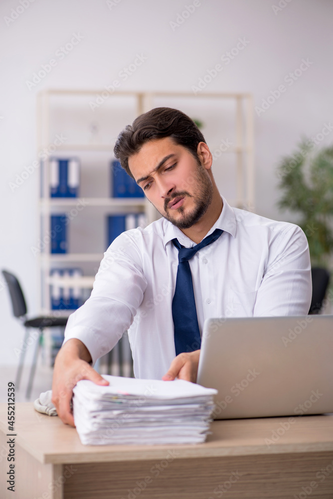 Young male employee unhappy with excessive work in the office Young male employee unhappy with excessive work in the office