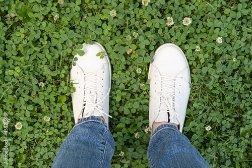 Legs in white leather sneakers on fresh green grass background. Nature walks in comfortable shoes.