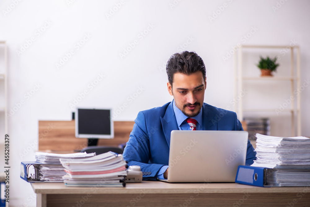 Young male employee unhappy with excessive work at workplace Young male employee unhappy with excessive work at workplace