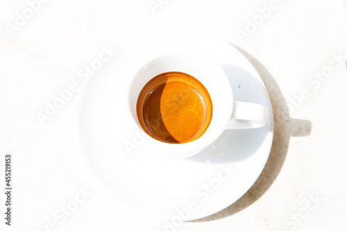 Round white coffee cup on white surface. High contrast picture. Traditional italian ristretto in bright summer day. Top view geometrical round composition. Hot caffeine beverage in a small cup.  photo