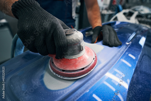 Sander grinding painted bumper in car workshop