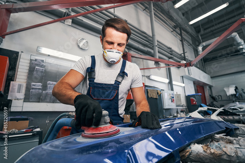 Positive automotive technician grinding automobile body part photo